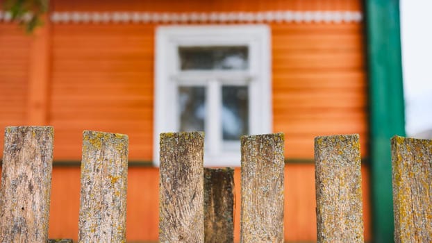 Weathered wooden fence bordering orange farmhouse, white window framing rustic countryside charm and nostalgic rural setting
