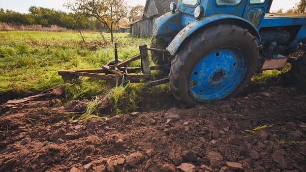 Old blue tractor working the fertile soil of a field, cultivating land and preparing for the upcoming sowing of crops