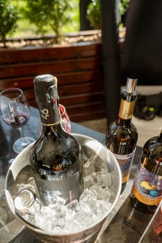 Odessa, Ukraine - April 05, 2025: A bottle of champange in an ice bucket at a hotel outdoors on a spring day. In the background, a bottle of wine and glasses. The blurred background includes a wine glass.