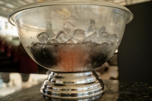 A glass bowl with ice. Ice cubes in a glass plate. A large bowl with ice for cooling bottles. High-quality photo