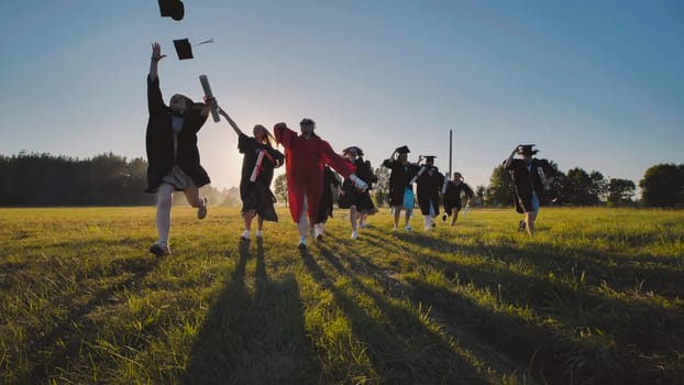 Group of cheerful graduating students running across field throwing their graduation caps in the air at sunset