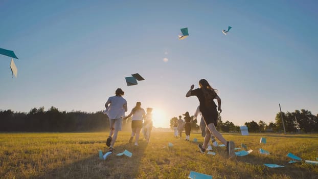 High school students rejoice in the end of the school year by sprinting through a field at sunset and tossing their notebooks into the air