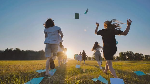 Group of teenagers running in a field throwing their notebooks in the air celebrating the end of school and the beginning of summer holidays
