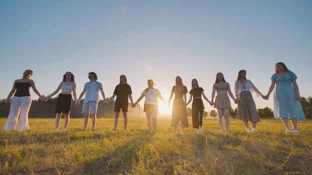 Group of young students linked together in a sunlit field at sunset, rejoicing in their summer break and cherishing the bond of friendship