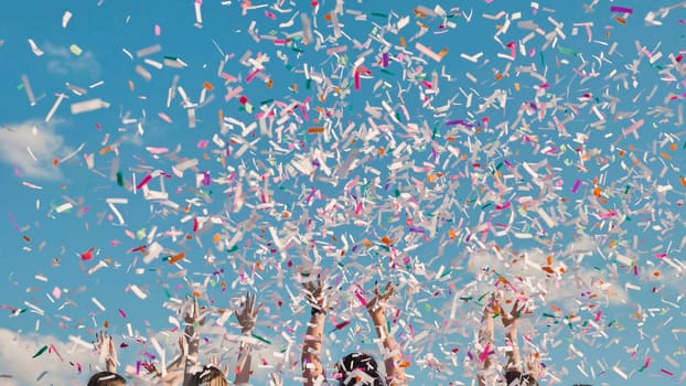 Group of cheerful students throwing colorful confetti in the air celebrating graduation day under a beautiful blue sky