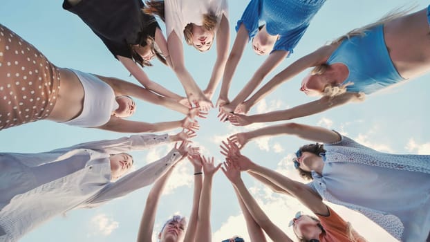Group of school friends forming a circle with their hands, demonstrating unity and teamwork against a bright sky