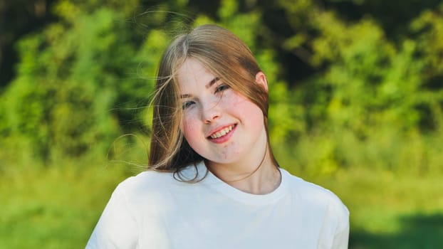 Blonde schoolgirl with freckles smiling in nature, enjoying summer holidays and expressing happiness
