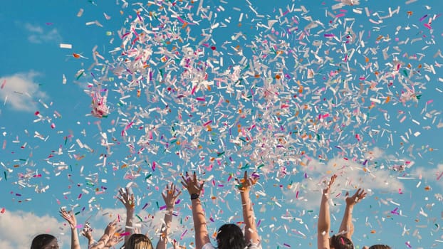 Group of high school students throwing colorful confetti in the air, celebrating their graduation under a bright blue sky
