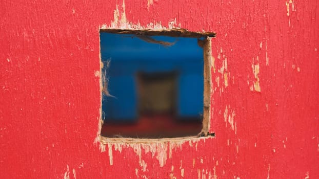 Square hole revealing blurred blue background in red painted wood