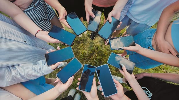 Students gathered in a circle on the grass, holding smartphones with blank screens, exchanging digital content and memories