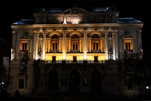 Front view of a grand historic theater at night, with classical columns, ornate statues, and warm architectural lighting.