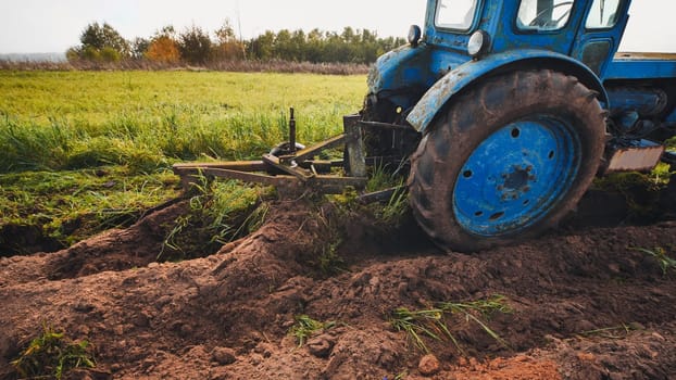 Old blue tractor plowing a field in autumn, creating furrows in the fertile soil, preparing for next season