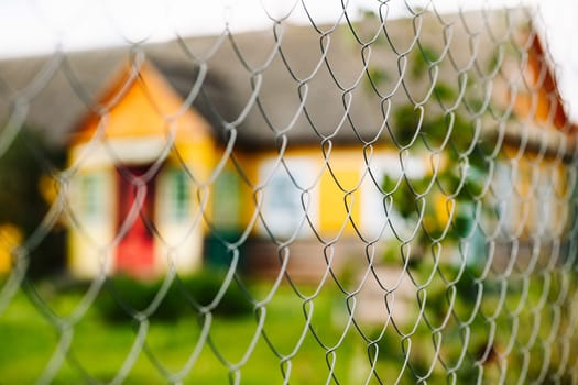 Metal mesh fence is separating viewer from colorful house with red door and green grass lawn