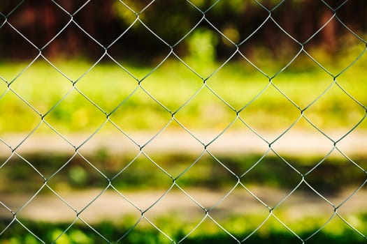 Close-up of a metal mesh fence with a blurred green background, creating a sense of separation and security