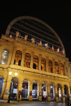 Lyon. France 04.20.2025 Nighttime view of a grand opera house with arched windows, classical statues, and modern glass dome, beautifully lit with warm lighting.