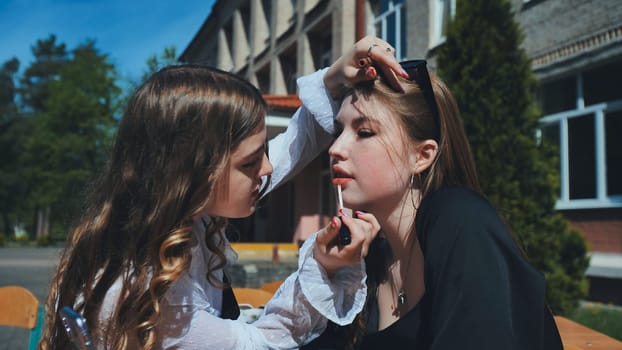 Schoolgirl applying lip gloss to her friend's lips in the schoolyard during the school day