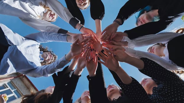 Group of students joining hands forming a circle, celebrating their school day achievement against a blue sky