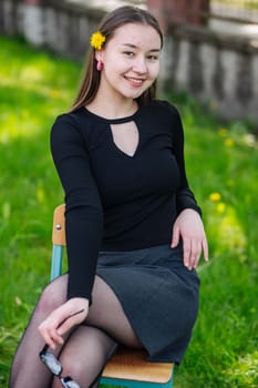 Smiling female student with dandelion in her hair, relaxing on a chair in the schoolyard during break time