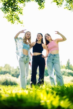 Three young women standing on grass making rock and roll hand gesture in a sunny summer day