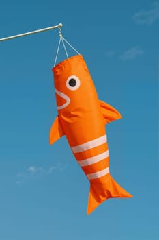 Orange fish-shaped windsock flying against blue sky. AI generation.