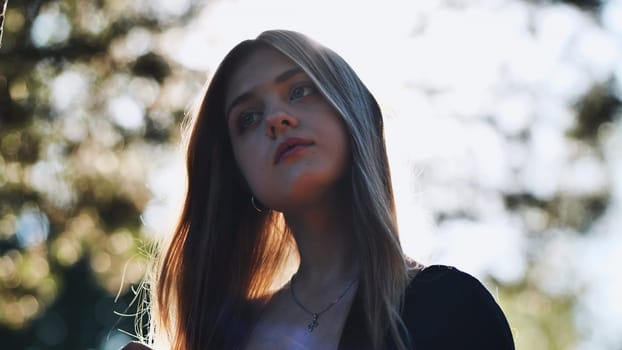 Portrait of a thoughtful teenage student with long hair, illuminated by sunlight filtering through trees, evoking contemplation and aspirations