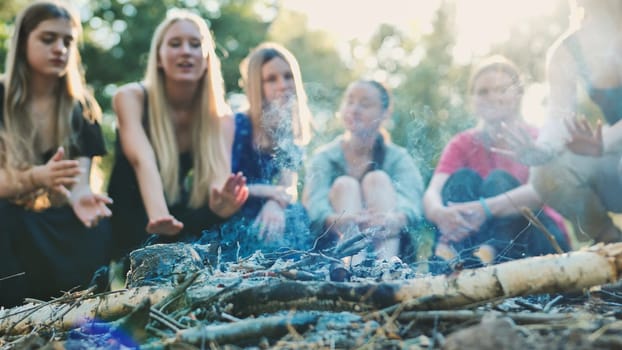 Group of school friends warming their hands around a small campfire during a camping trip