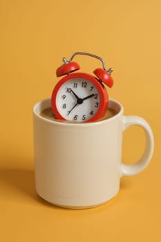 Red alarm clock placed inside large ceramic coffee mug. AI generation.