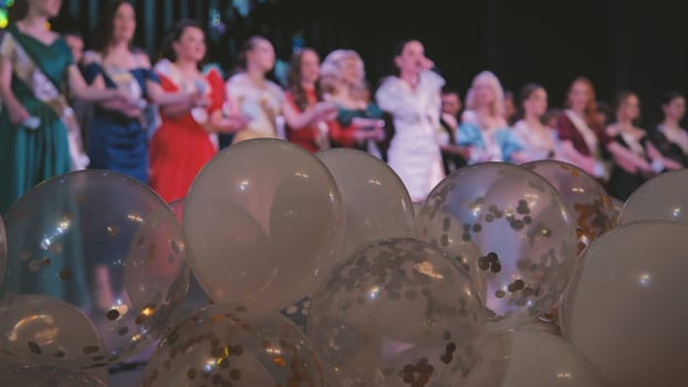 Multicolored graduation balloons floating, falling confetti, celebrating students clapping joyfully in background