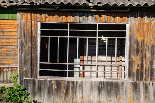Barred window on weathered wooden facade of derelict building, showing decay and neglect