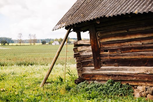 Weathered wooden barn with slate roof slowly collapsing in overgrown field near wire fence