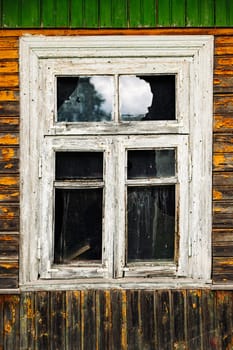 Broken window with peeling paint in old abandoned wooden house reflecting cloudy sky