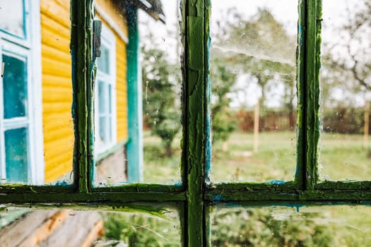Dirty window glass with peeling paint showing a colorful house and garden
