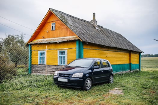 Small family car parked near a yellow and green wooden house in the countryside, representing simple living and rural lifestyle
