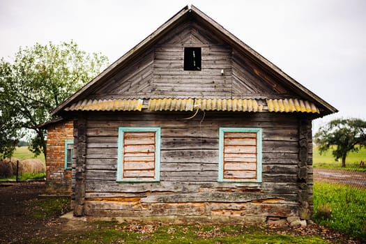 Weathered wooden facade of an old abandoned house with broken windows in a rural landscape