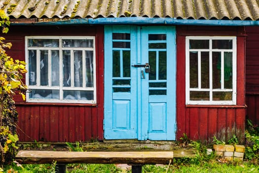 Charming tiny house with light blue door and white windows, with a wooden bench in front of it