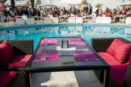 Odessa, Ukraine - April 05, 2025: City street food festival near hotel in swimming pool area. People and tables set for food around the pool. Table with reserved sign in foreground