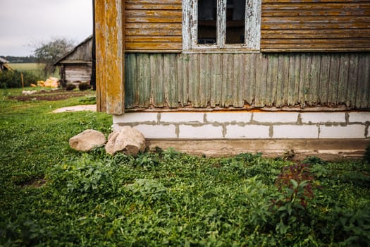 Weathered wooden house with a new foundation made of concrete blocks and plants growing around