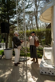 Odessa, Ukraine - April 05, 2025 : city spring fair. Two well-groomed and stylish seniors drink wine and chat. glasses of wine in hands.