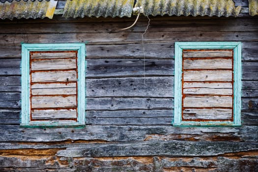 Two boarded windows with decaying green frames on the weathered wall of an abandoned wooden house