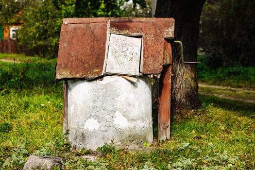 Rusty abandoned water well slowly decaying in the summer countryside near a tree