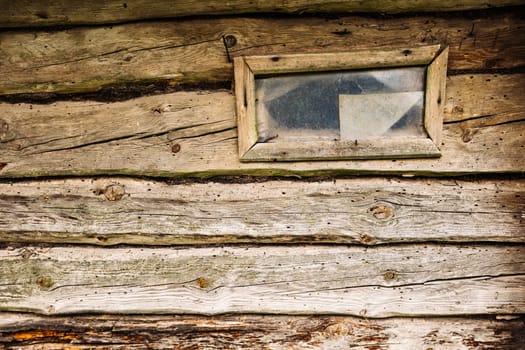 Old weathered wooden planks and a small window with broken glass are creating a rustic background