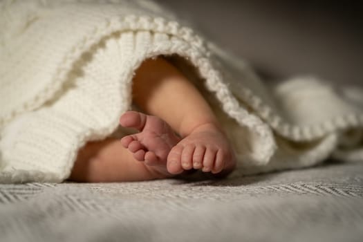Tiny baby feet are visible as they peek out from a soft white knitted blanket, creating a warm and serene atmosphere in a cozy home setting.