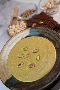 Rich pistachio cream is served in an elegant bowl, garnished with nuts, alongside chocolate pieces and additional nuts in Dubai's vibrant culinary scene.