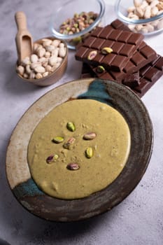 Rich pistachio cream is served in an elegant bowl, garnished with nuts, alongside chocolate pieces and additional nuts in Dubai's vibrant culinary scene.