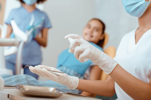Disinfection of medical equipment. Focus on millennial woman doctor in rubber gloves and protective mask processes dental instruments, before examination of smiling little girl in armchair, cropped