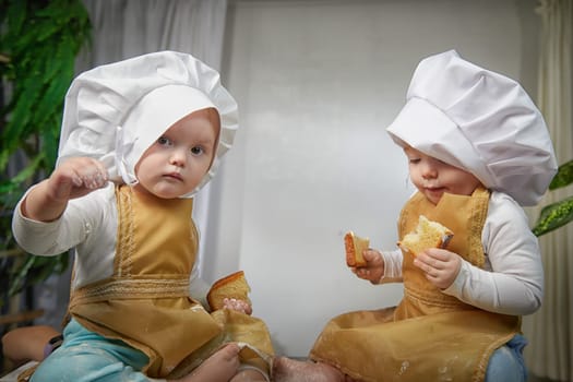 Two toddlers dressed as chefs delight in playful baking session, surrounded by flour and treats, sharing laughter and joy