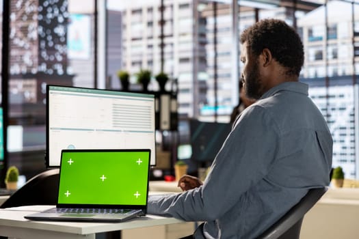 Male business manager at desk looking at mockup screen and solving tasks for company objectives accomplishment. Fighting for performance goals to ensure successful corporate outcomes.