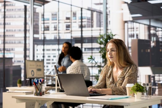 Confident businesswoman working at a desk in corporation, reviewing financial reports on her laptop. Successful employee managing business tasks and developing a strategy plan for the company.
