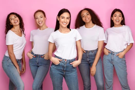 Five Pretty Mixed Young Ladies Standing And Smiling To Camera Posing On Pink Background In Studio, Wearing Casual Clothes T-Shirts And Jeans. Happy Females Group, Multiethnic Beauty Concept