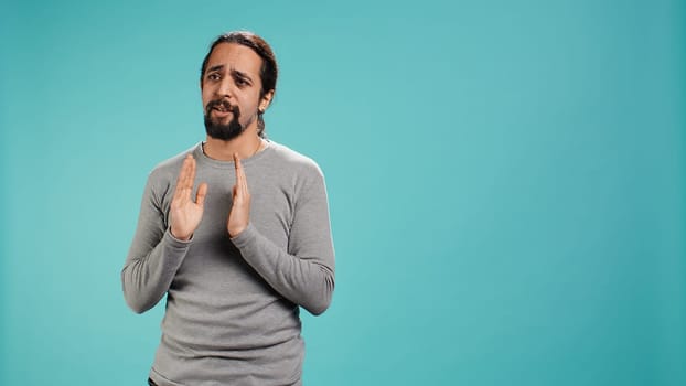 Man putting hands together in begging gesture, making wish, asking for favor from friend, isolated over studio background. Desperate person asking for something, praying and hoping, camera B